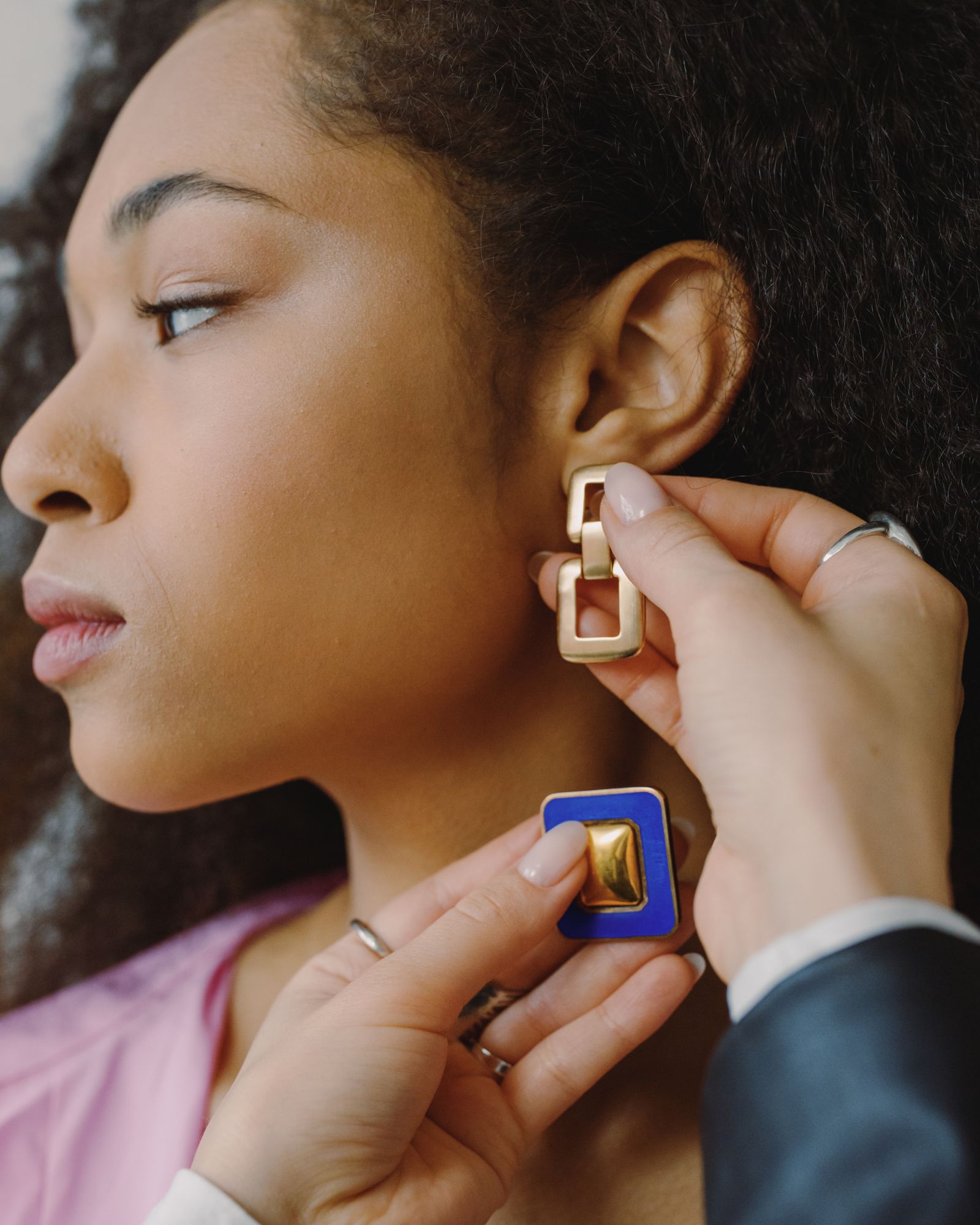 A woman trying on geometric gold earrings.