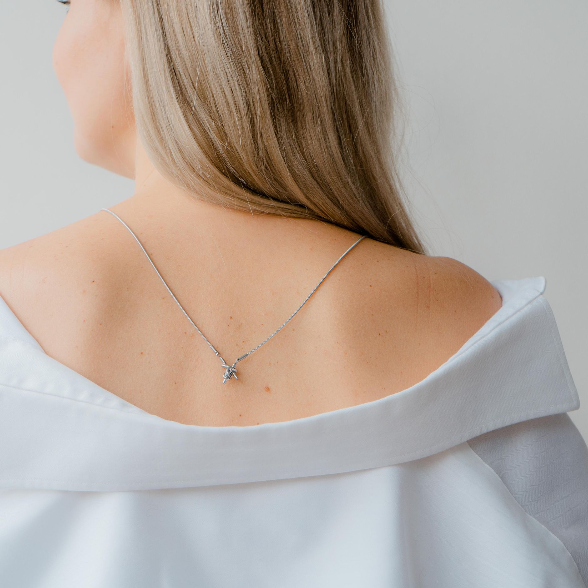 A woman seen from behind wearing a fine necklace and a white shirt.