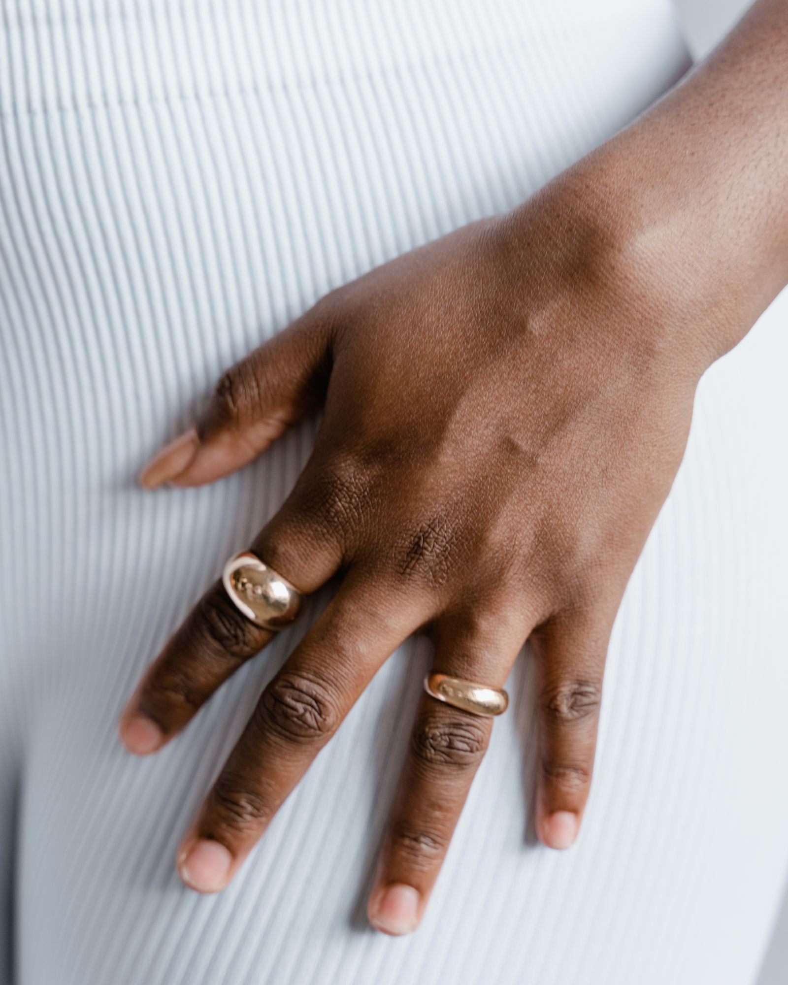 A hand wearing slim gold rings against a white textured background.