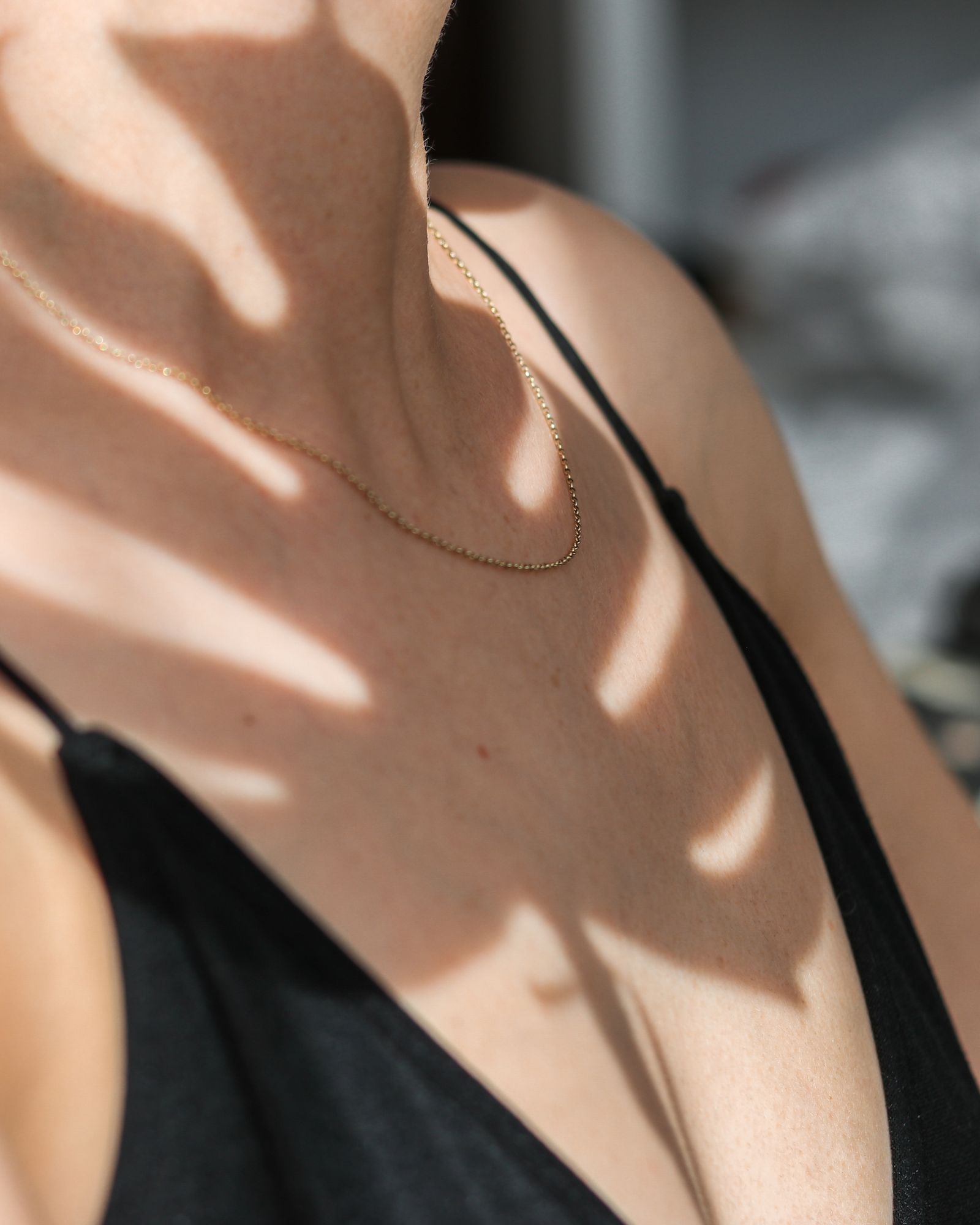 A gold pendant necklace on a woman's neck with soft shadows.