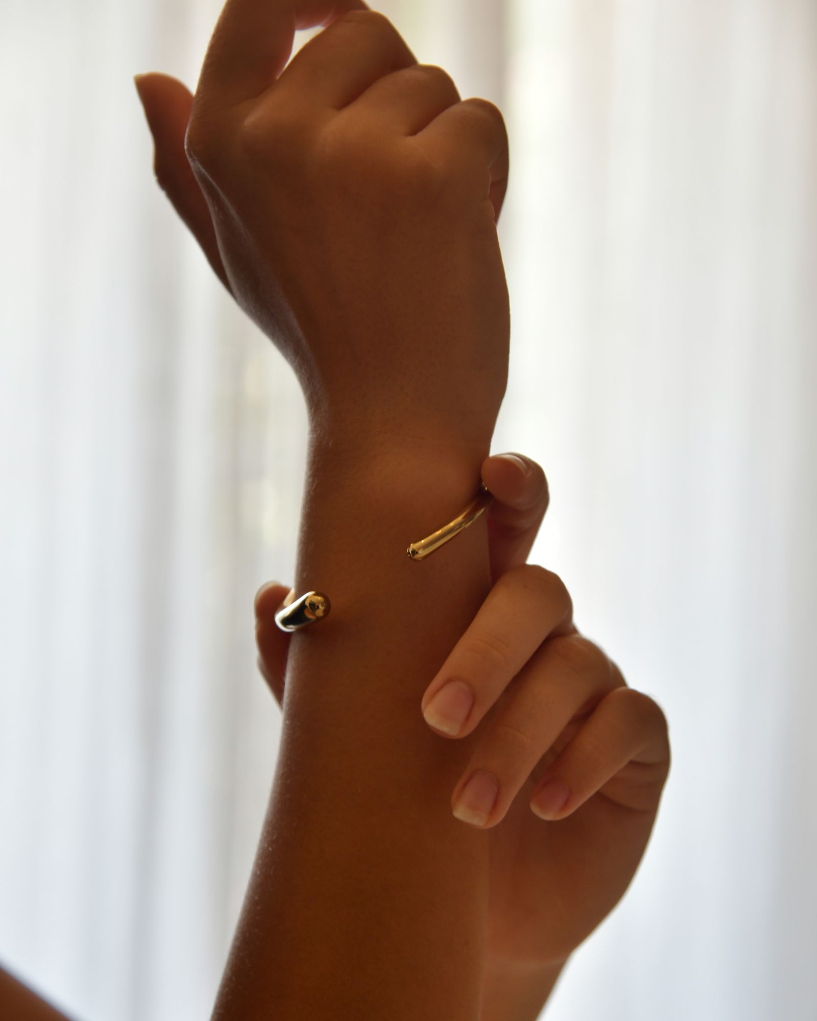 A minimalist gold bracelet on a woman's wrist in soft light.