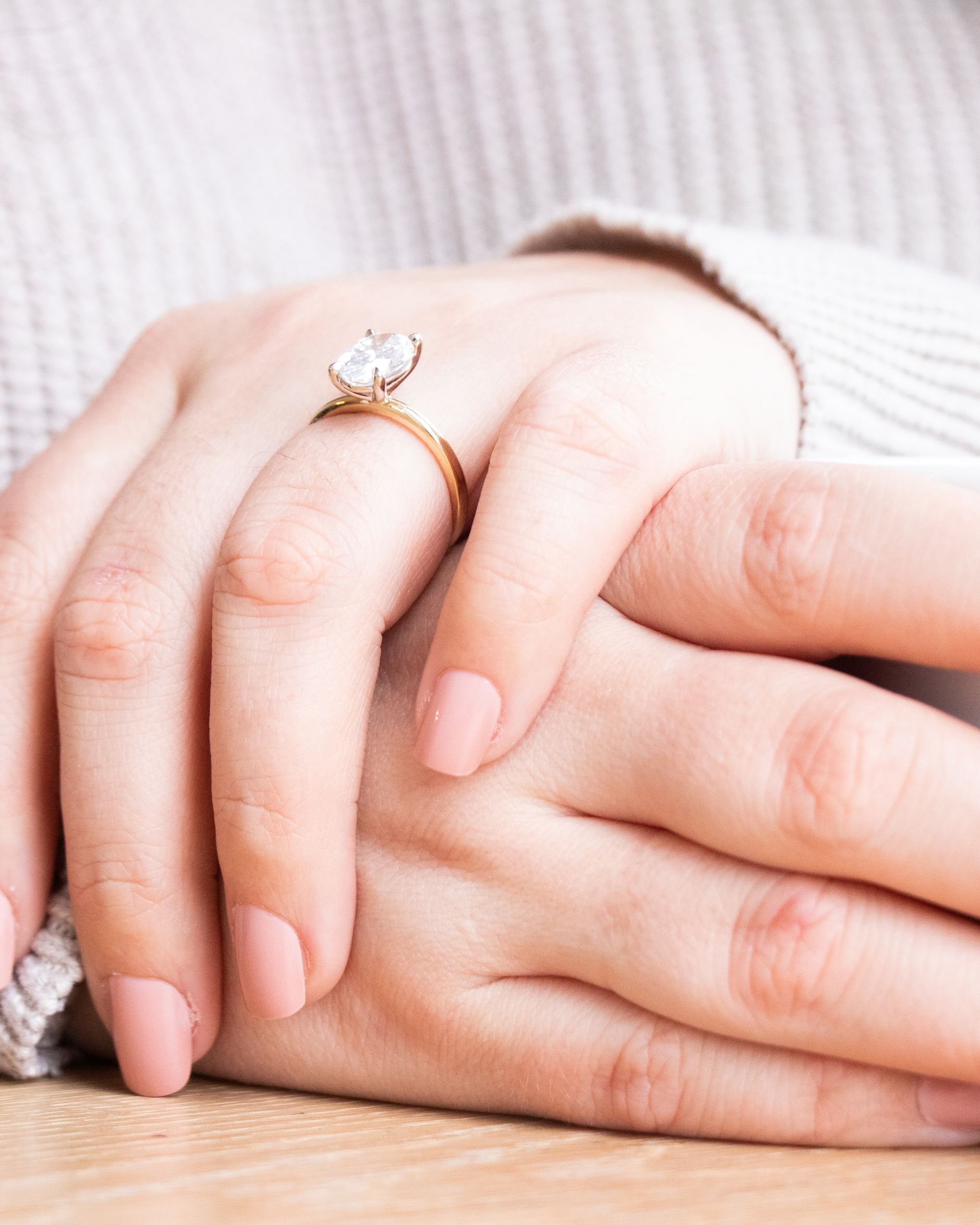A hand with a slim ring resting beside a coffee cup.