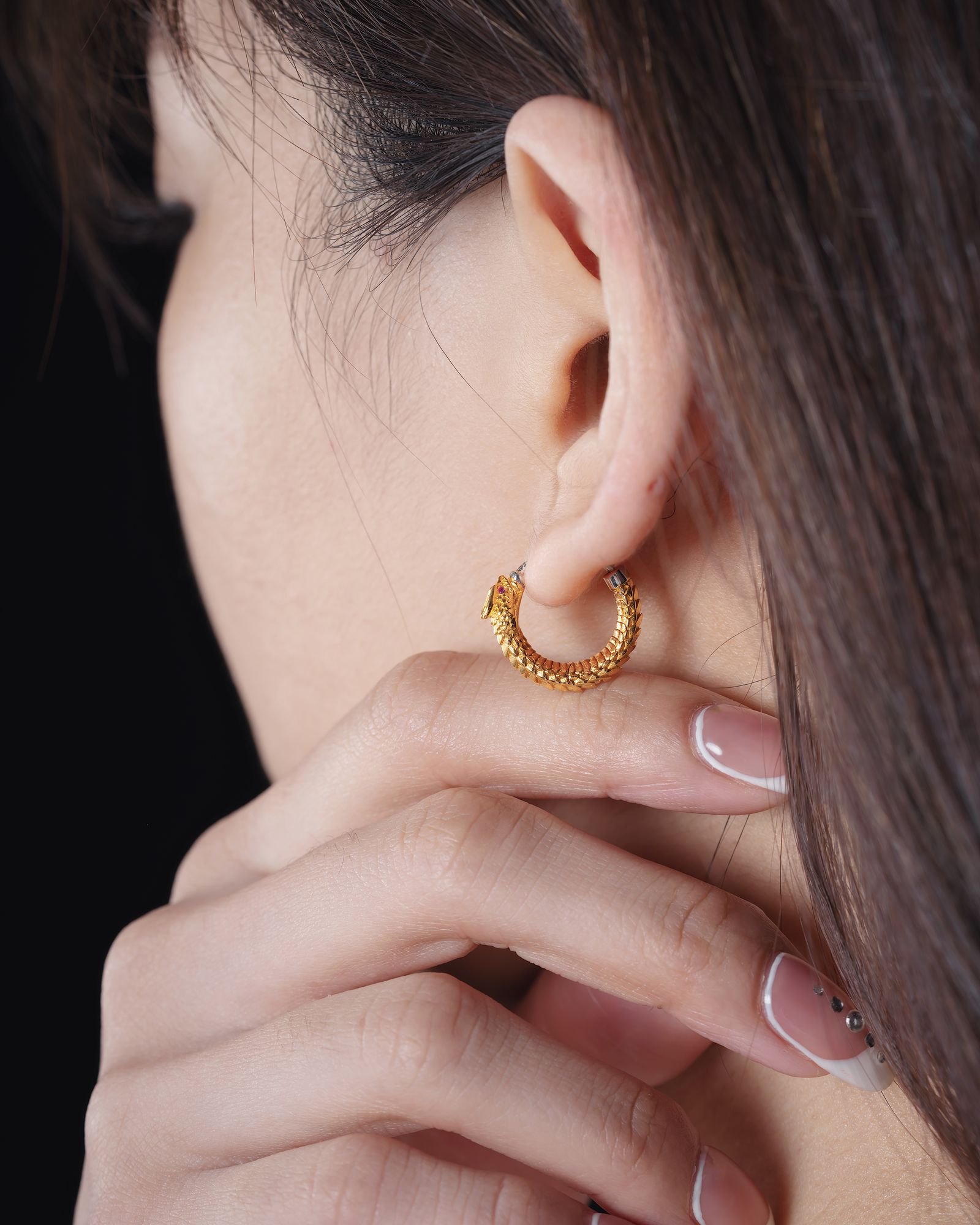 A textured gold earring worn close up.