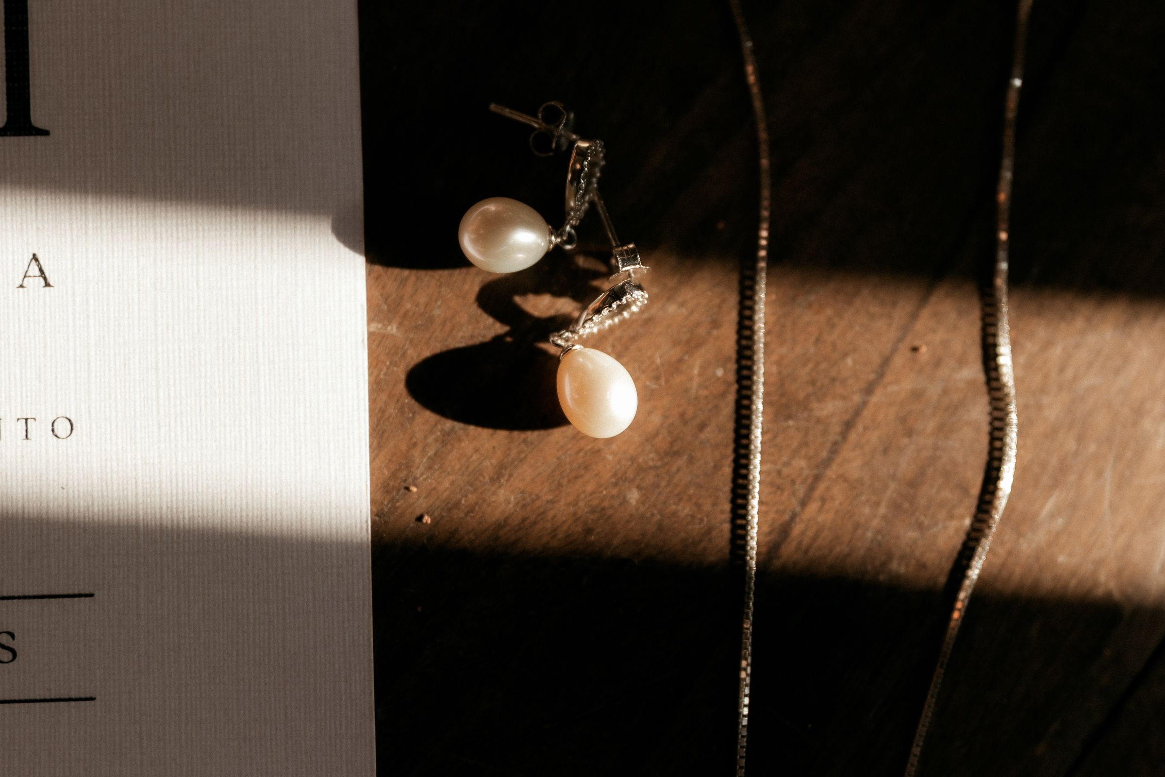 Pearl earrings and a fine chain on a wooden surface.